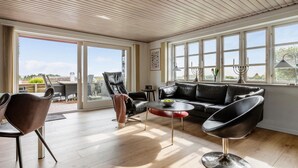 A spacious living room with a large window, a leather sofa, a coffee table, and a dining area with chairs. - Pet friendly home in Slagelse with WiFi (Slagelse)