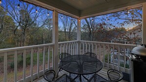 A covered outdoor patio with a round table and chairs, surrounded by a white railing. - Sunset Cottage (Fairfield Bay)