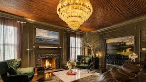 Ein Zimmer mit Kamin, Ledersofas, einem Chandelier und Kunstwerken an den Wänden.