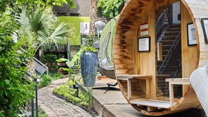 Ein holzgestelltes Zimmer im Pod-Stil mit integriertem Ventilator, einer Treppe und Blick auf einen üppigen Garten.