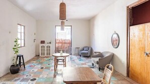A spacious room with a tiled floor, a wooden table, a chair, a sofa, a hanging light fixture, and a door. - Twin Room on 5th A06 (Playa del Carmen)