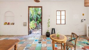 A room with a colorful tiled floor, a wooden table with chairs, a potted plant, and a doorway leading to an outdoor area with plants. - Twin Room on 5th A06 (Playa del Carmen)