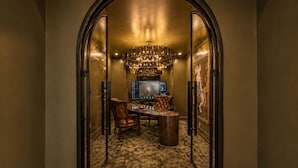 Un arco de entrada conduce a un comedor con una araña, un televisor y una obra de arte enmarcada en la pared.