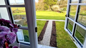 A view through a window with a white frame, a wooden fence, and a grassy area with a gravel path. - 2 x 3 Bedroom houses side by side quiet peaceful location , Amazing views. (Marazion)