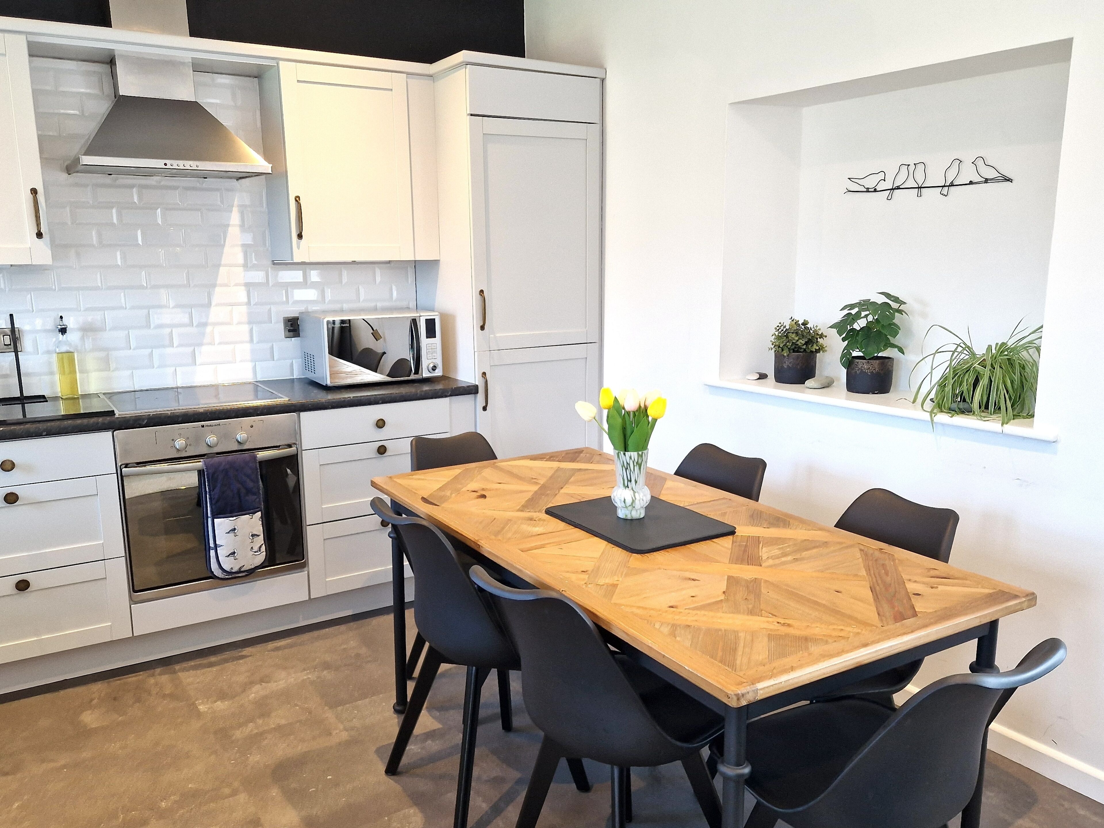 Une cuisine moderne avec des meubles blancs, un four à micro-ondes encastré et une table à manger en bois avec des chaises noires.
