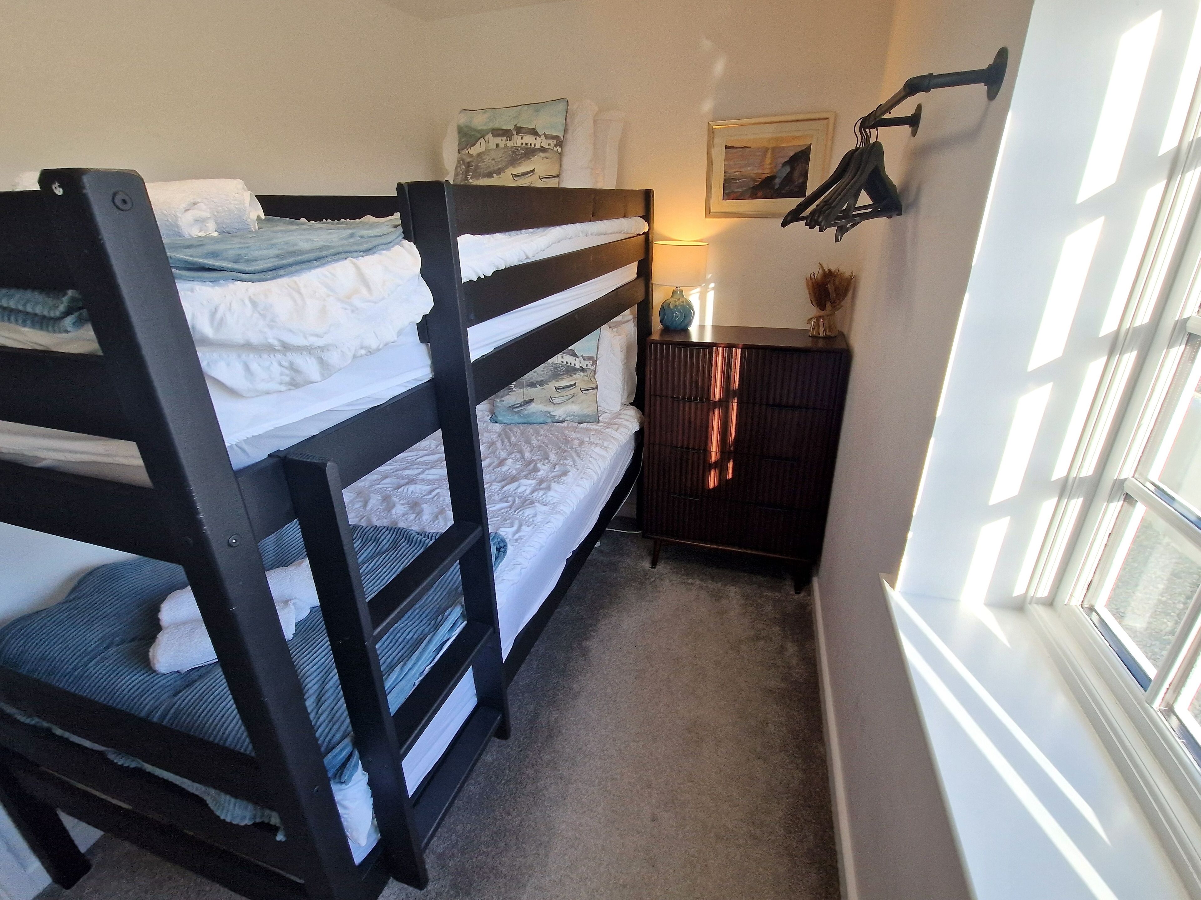 A room with bunk beds, a dresser, a lamp, and a window with blinds.