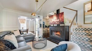 A modern living room with a fireplace, leather sofas, a coffee table, and a staircase with patterned carpet.