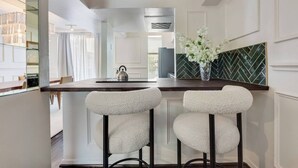 A modern kitchen with two bar stools, a kettle, and a vase with flowers on the counter.