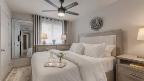 A neatly arranged bedroom with a bed, bedside tables, a ceiling fan, and a large mirror.