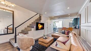 A spacious living room with a fireplace, comfortable seating, a staircase, and a view into the dining area.