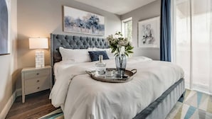 Un dormitorio ordenado con una cama grande, una mesita de noche, una bandeja con vasos y obras de arte en las paredes.