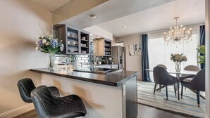 Una cocina moderna con una isla central, taburetes de cuero negro y una lámpara de araña.