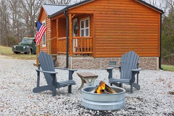 Une cabane en bois avec deux fauteuils Adirondack et un foyer à l’extérieur.