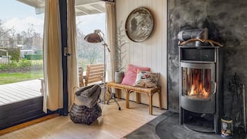 Ein gemütliches Zimmer mit Kamin, einem Korbstuhl, einer Bank und Blick durch eine Glastür.