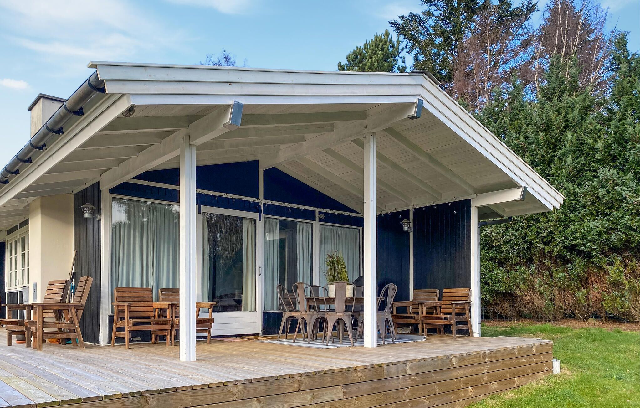 Ein überdachter Außenbereich mit Holzterrasse, einem Tisch mit Stühlen und einem Blumentopf.