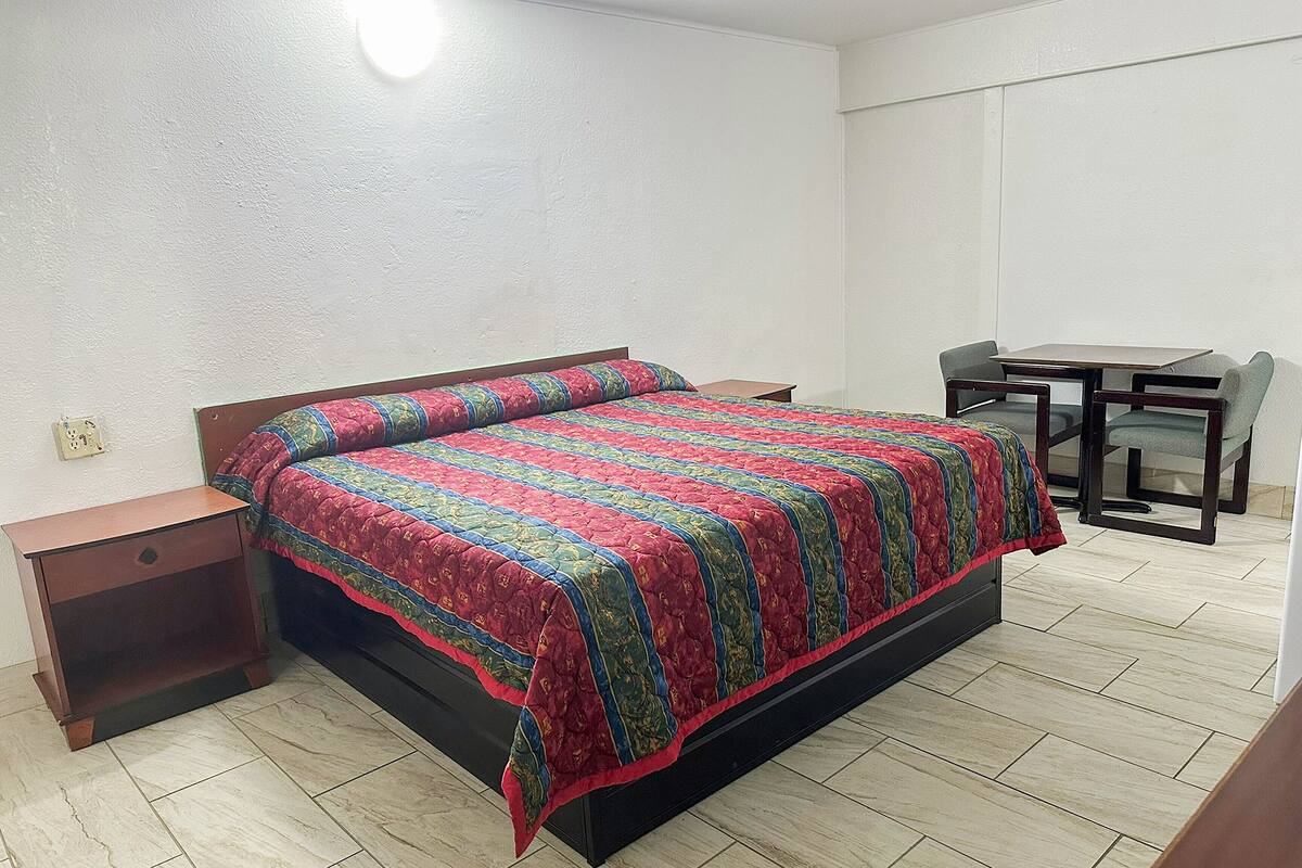 A bedroom with a bed, a nightstand, a desk, and a chair.