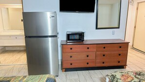 A compact living space with a refrigerator, microwave, wooden dresser, and a television mounted on the wall.