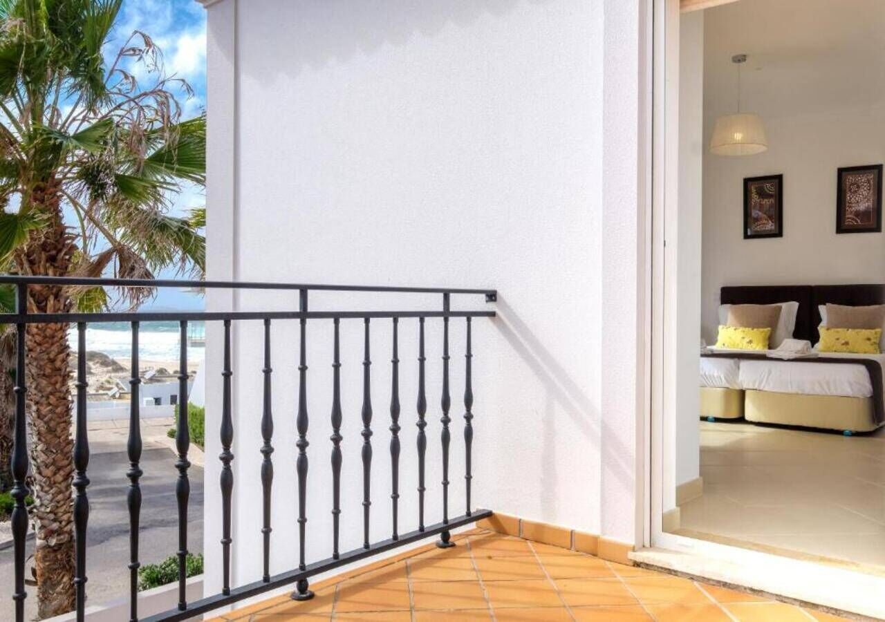 Un balcon avec une balustrade noire, un palmier et une vue sur la plage.