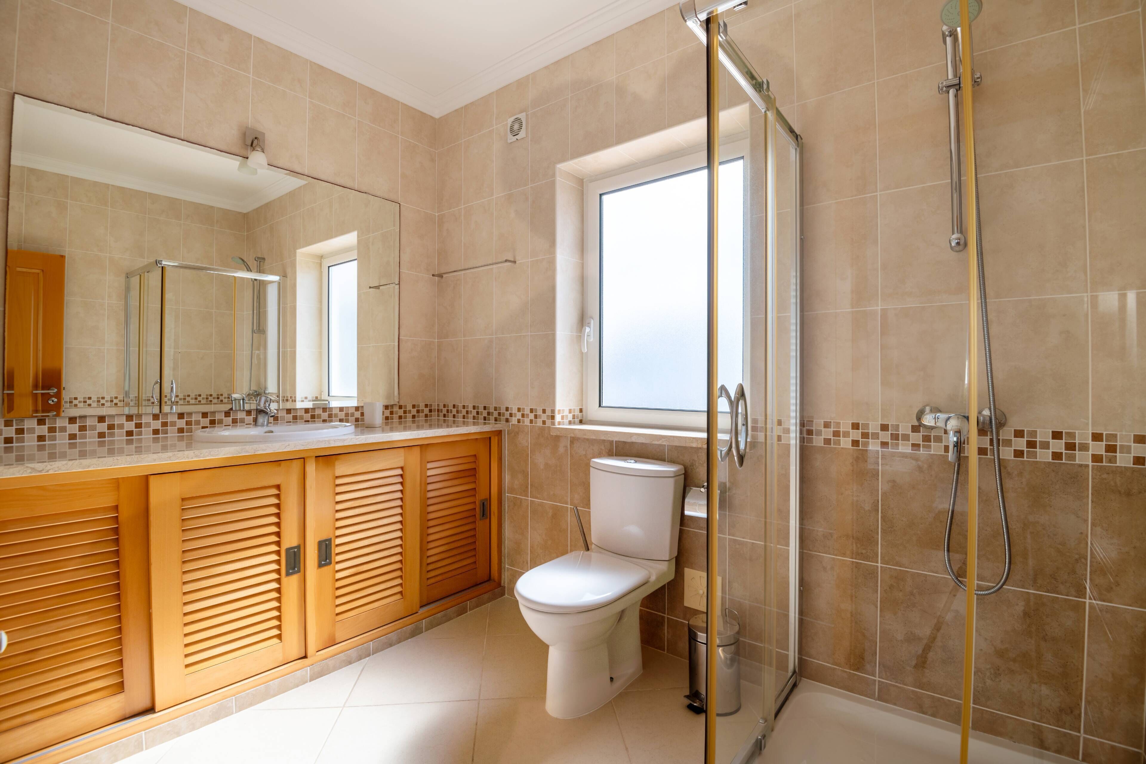 Ein modernes Badezimmer mit einer gläsernen Duschkabine, einer Toilette und einem Waschbecken mit Holzschrank.