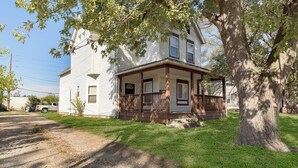A two-story house with a porch, a large tree in front, and a dirt driveway.