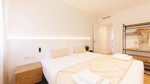 Una habitación de hotel moderna con una cama grande, una mesita de noche de madera, un espejo y un armario con ropa colgada.