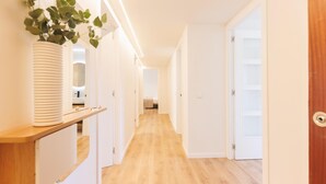 Un pasillo con suelo de madera, paredes blancas y una planta en un estante.