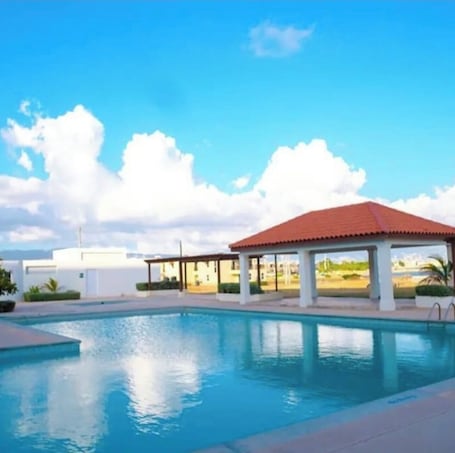A swimming pool with a gazebo, a clear sky, and a distant view of buildings.