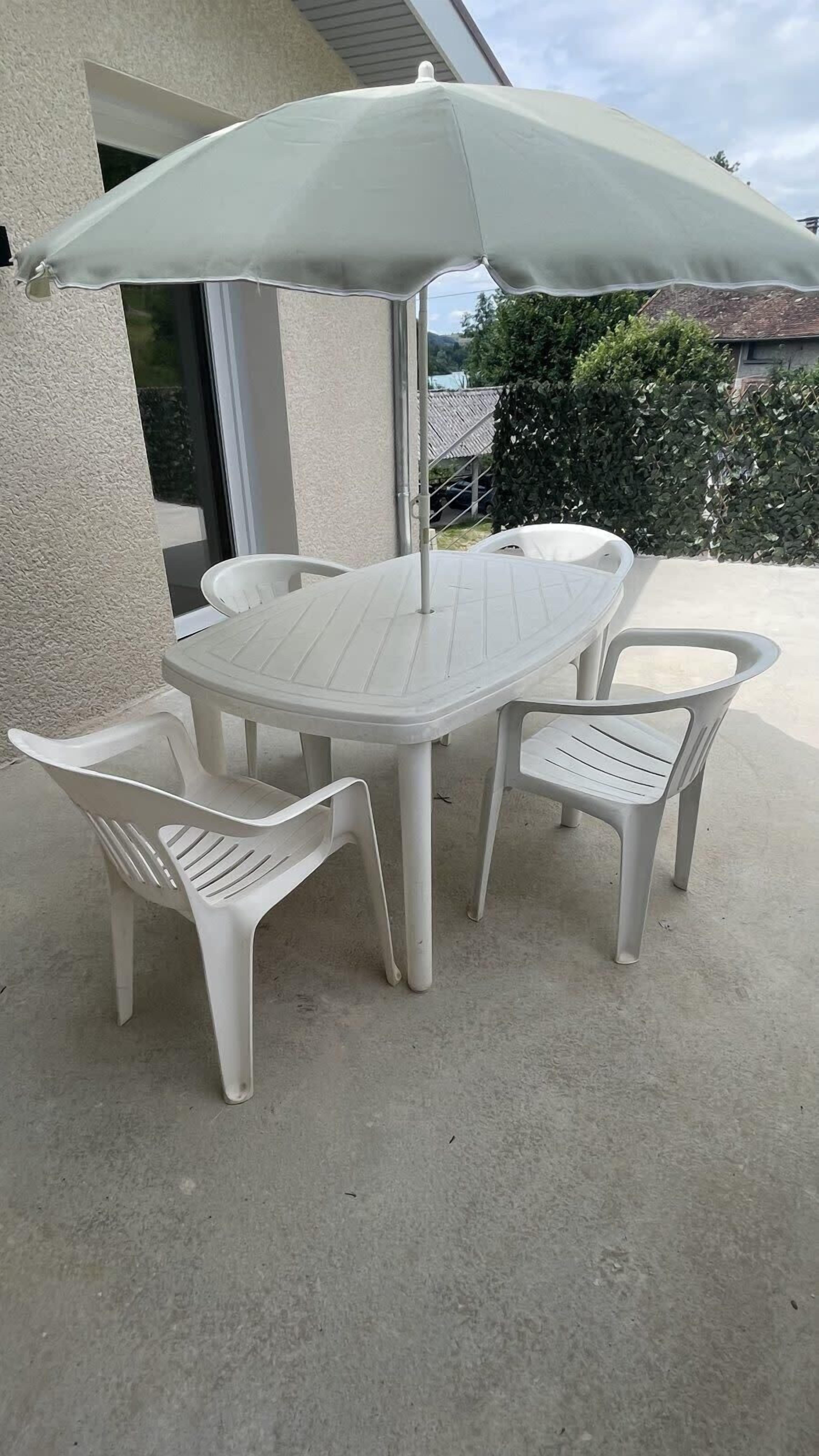 A patio table with a white umbrella, surrounded by white plastic chairs.