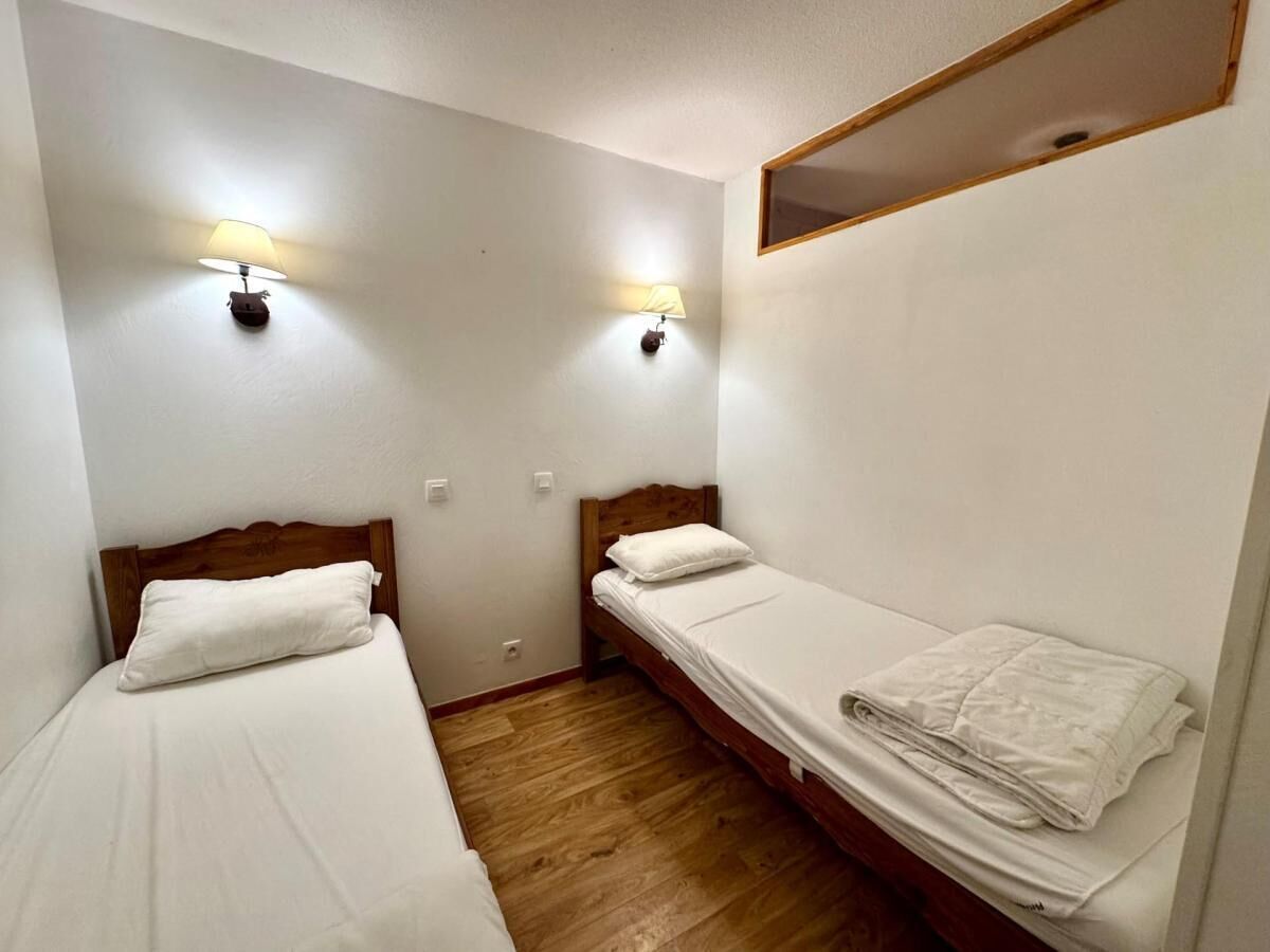 A small, clean room with two single beds, wooden headboards, and two wall-mounted lamps.