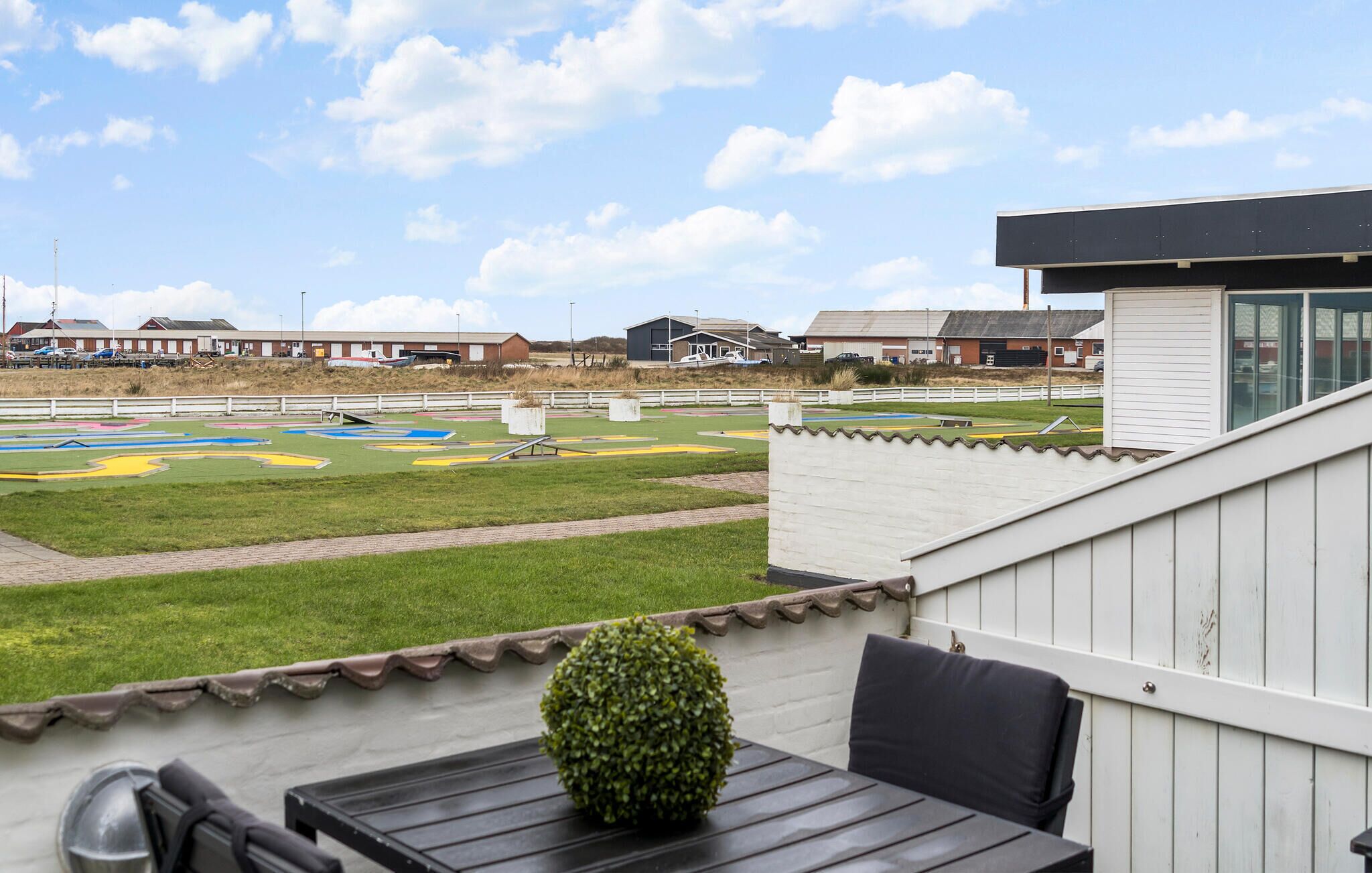 Un patio con una mesa y sillas, con vista a un área verde con diseños coloridos y un edificio al fondo.