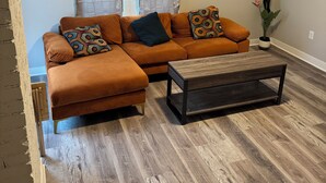 A living room with a sectional sofa, a coffee table, and decorative wall art. - Charming 2-bedroom house with AC, WiFi in Columbus (Columbus)