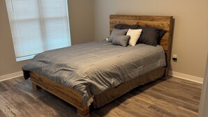 A bedroom with a wooden bed frame, a grey bedspread, and a window with blinds. - Charming 2-bedroom house with AC, WiFi in Columbus (Columbus)