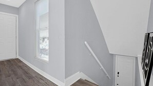 A hallway with a white door, a window with blinds, and a staircase with a handrail. - Charming 2-bedroom house with AC, WiFi in Columbus (Columbus)