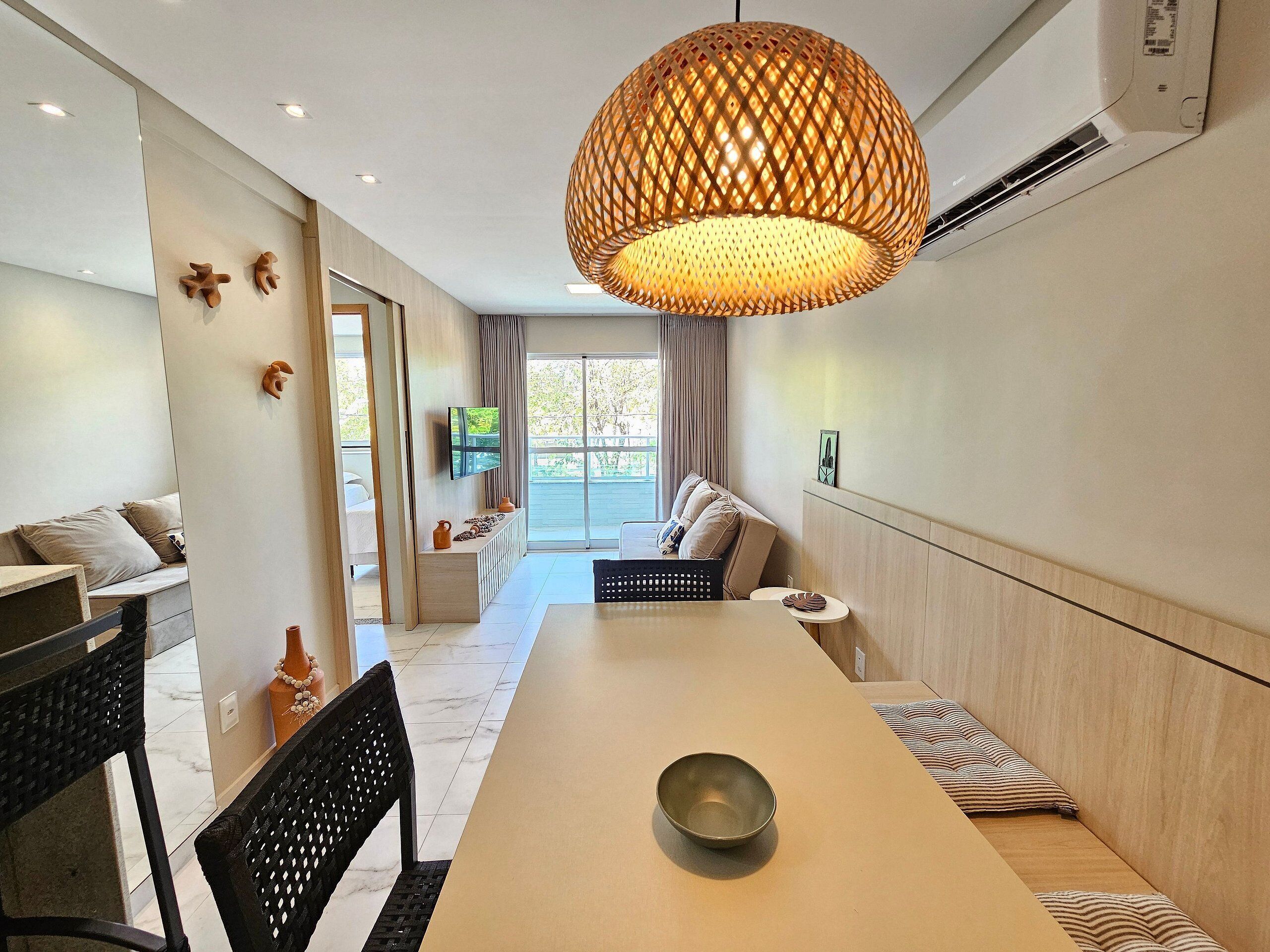 A modern dining area with a long table, black chairs, and a woven pendant light.
