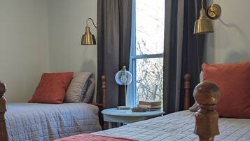 A bedroom with two beds, a small table, and a window with curtains.