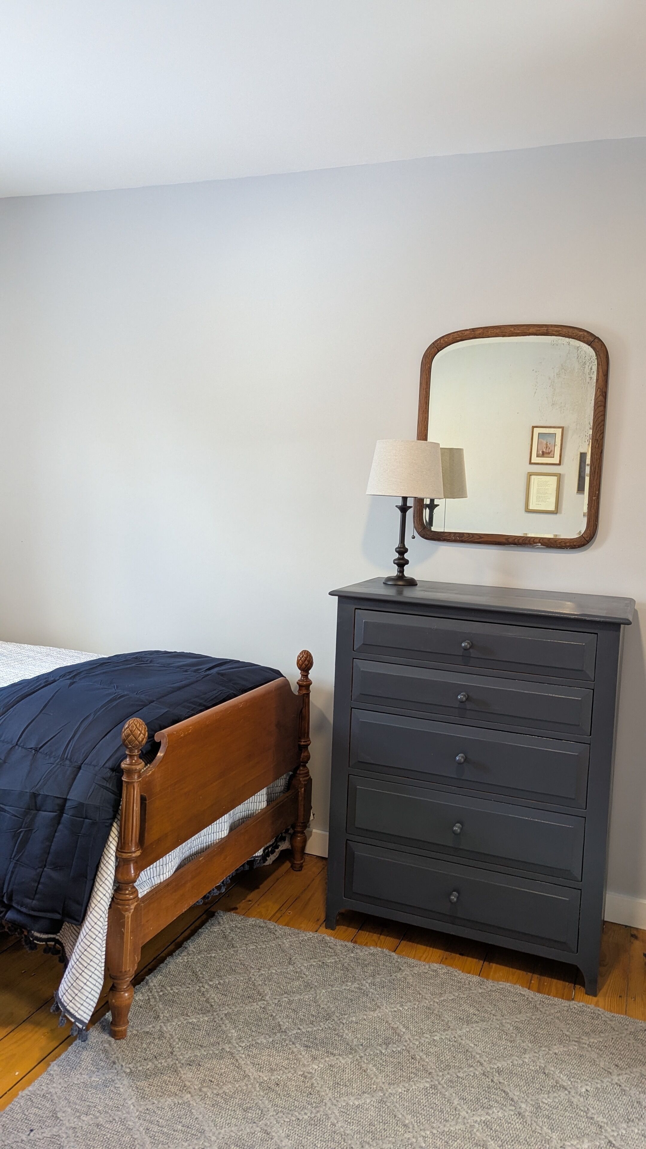 A bedroom with a wooden bed, a grey dresser, a mirror, and a lamp.