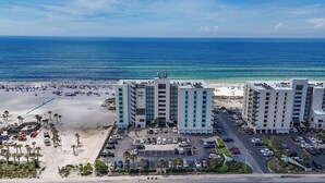 Un hotel frente a la playa con varias construcciones, un estacionamiento y una playa al fondo.