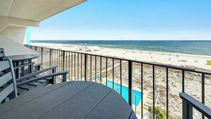 Un balcón con vistas a una playa, una piscina y una mesa.