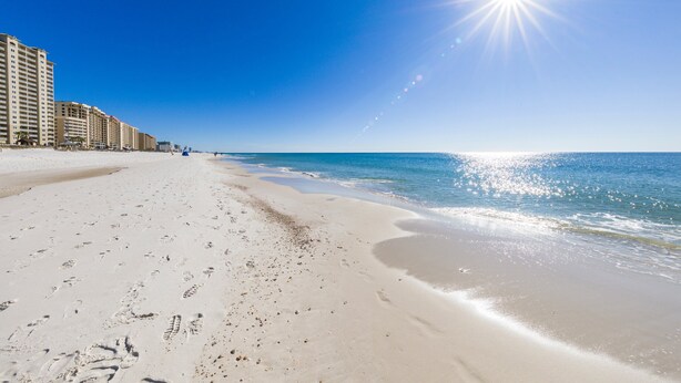 A beach with footprints leading to a building complex. - Romar Place 702 | Spectacular Gulf Views Oceanfront Condo | Beach Getaways (Orange Beach)