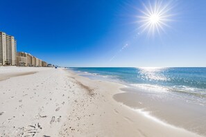 A beach with footprints leading to a building complex. - Romar Place 702 | Spectacular Gulf Views Oceanfront Condo | Beach Getaways (Orange Beach)