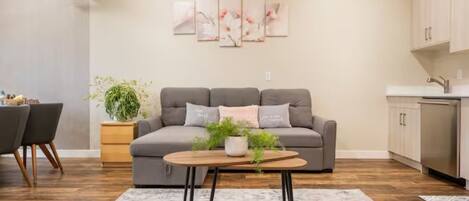A modern living room with a grey sofa, a coffee table, and a dining area with chairs and a table.