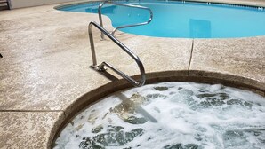 Una piscina con un jacuzzi en primer plano, un banco y una silla de salvavidas.