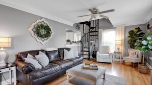 A modern living room with a leather sofa, a white armchair, a wooden coffee table, and a spiral staircase leading to an upper level. - Charming 3br Property with fenced in downtown Mooresville, NC (Mooresville)