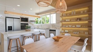 Una cocina moderna con armarios blancos, una isla central con taburetes y una mesa de comedor con sillas.