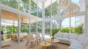 Un salón amplio con ventanas grandes, un sofá blanco, sillas de madera y una mesa redonda.