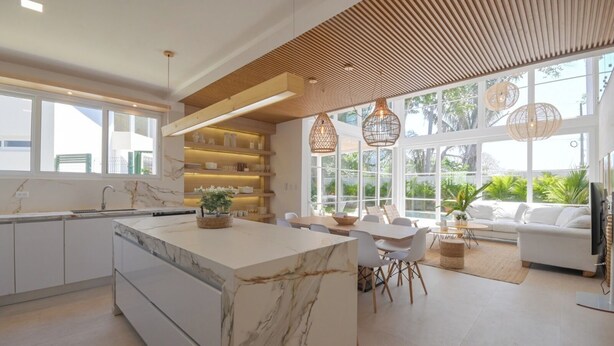 Una cocina moderna con una isla de mármol, estantes de madera y ventanas amplias.