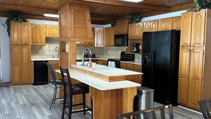 A kitchen with wooden cabinets, a black refrigerator, a microwave, and a sink. - Luxury Estate Accommodations, with a Serene Pool, and Elegant Event Spaces (Douglasville)