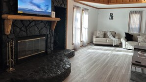 A living room with a stone fireplace, a mounted TV, and a wooden ceiling. - Luxury Estate Accommodations, with a Serene Pool, and Elegant Event Spaces (Douglasville)