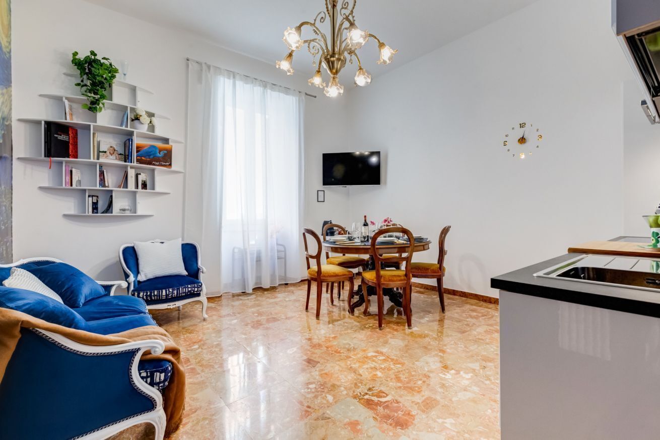 A modern living room with a sofa, dining table, chairs, a TV, and a kitchen area.