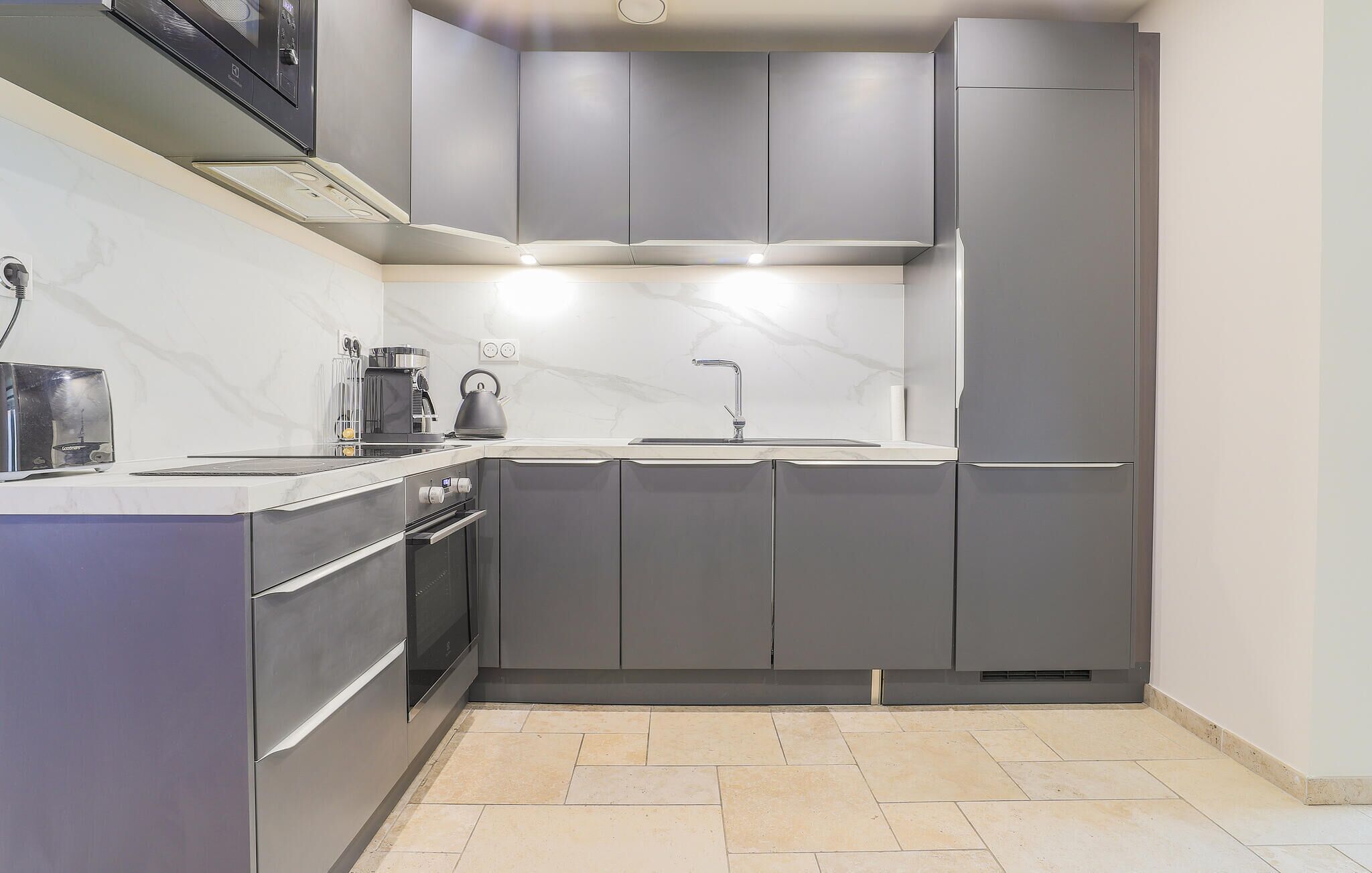 Een moderne keuken met grijze kastjes, een ingebouwde oven, een waterkoker en een koffiezetapparaat.